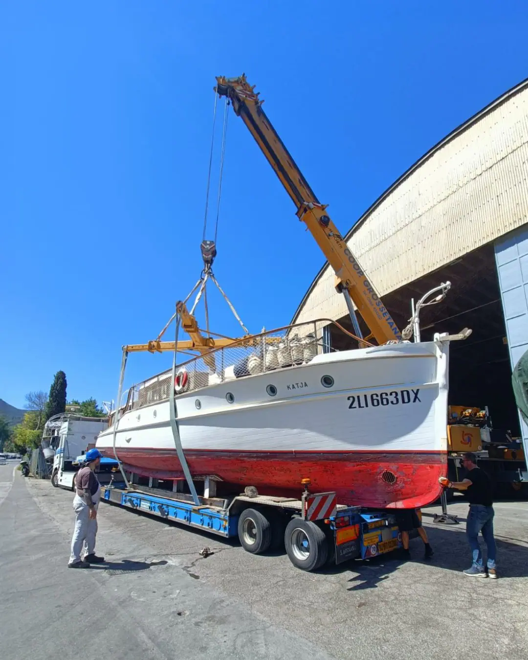Il motor yacht Katya 1929 sollevato da una gru su un rimorchio, durante il trasporto fuori dal cantiere navale